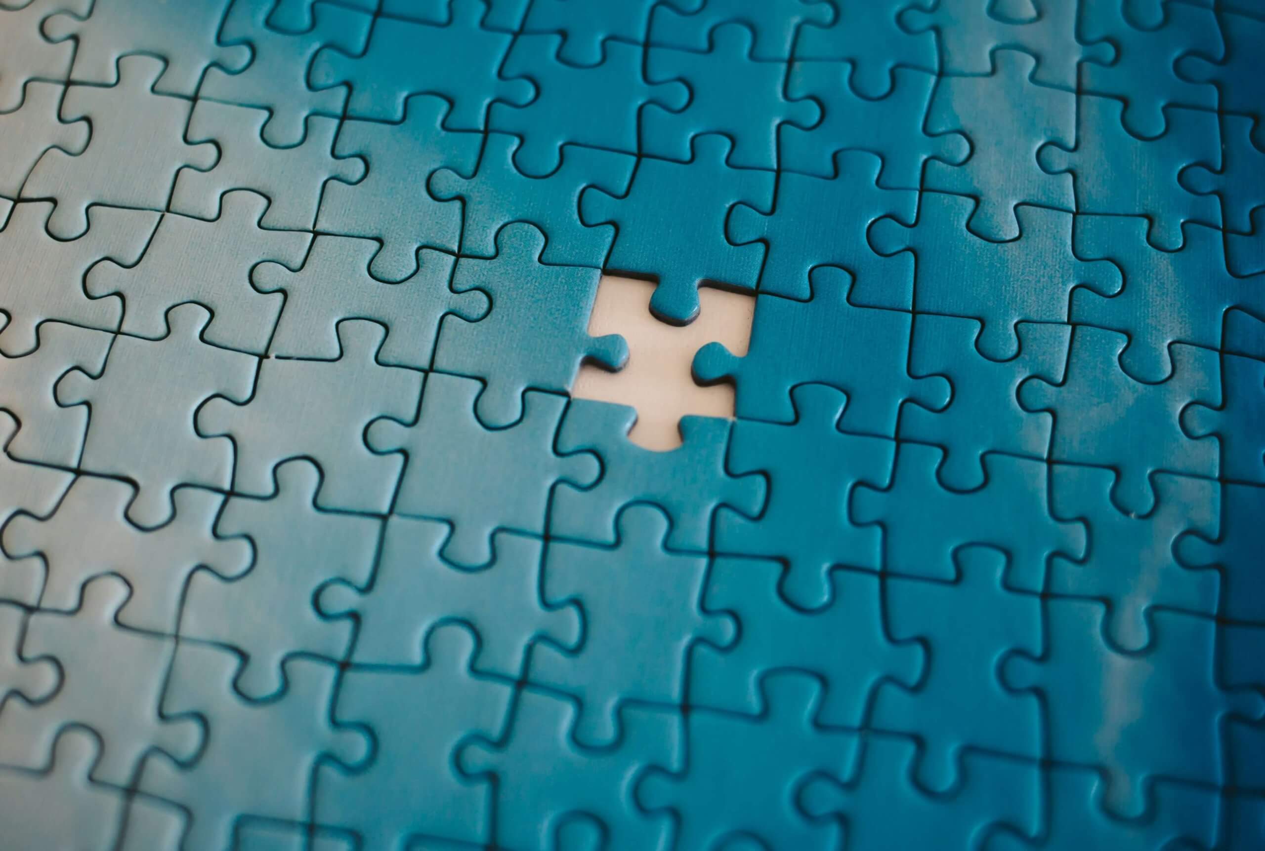 A nearly completed blue jigsaw puzzle with one missing piece in the center, symbolizing an incomplete system or a gap in a unified solution
